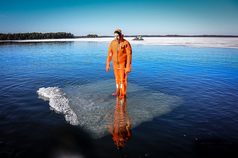 Person wearing an orange survival suit and standing on a floating ice raft